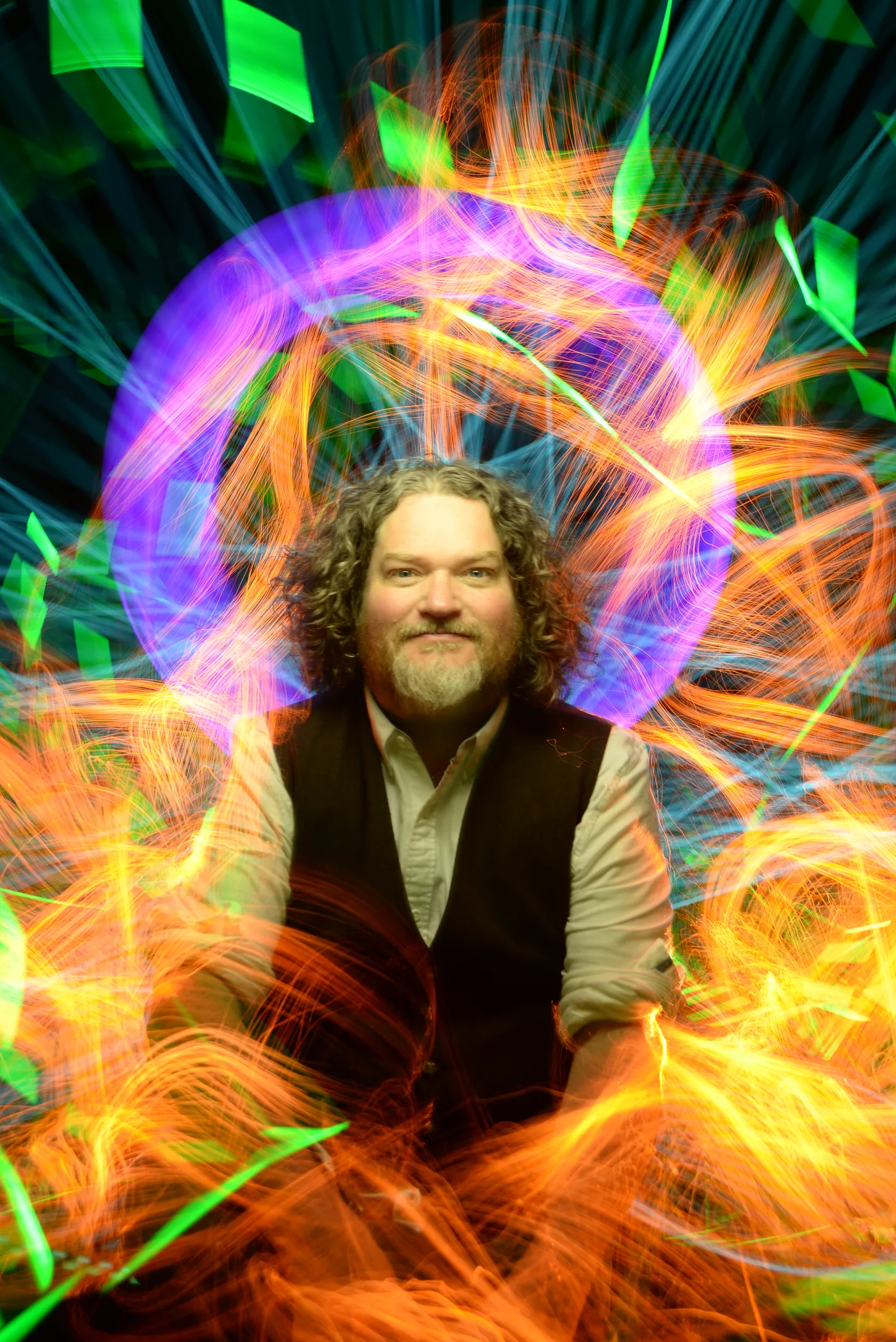 Tor Webster smiling, seated inside swirling orange, purple and green light painting