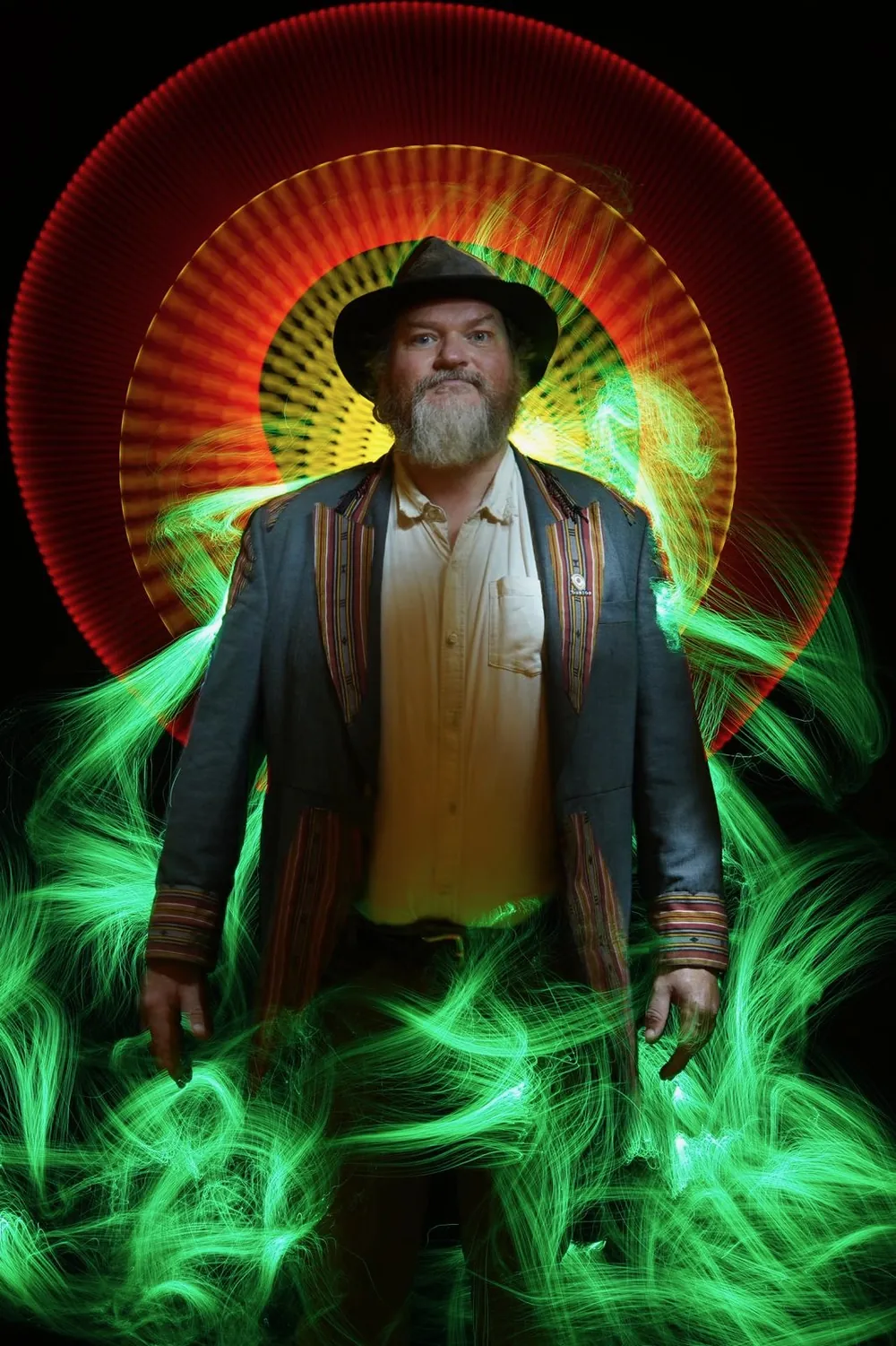 Tor Webster in a hat and striped jacket, framed by a red halo of light and swirling green light painting