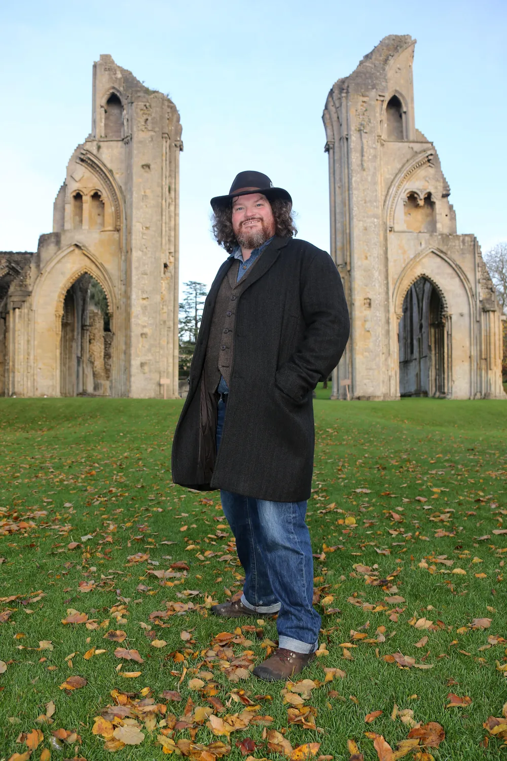 Tor Webster standing before the ruined towers of Glastonbury Abbey
