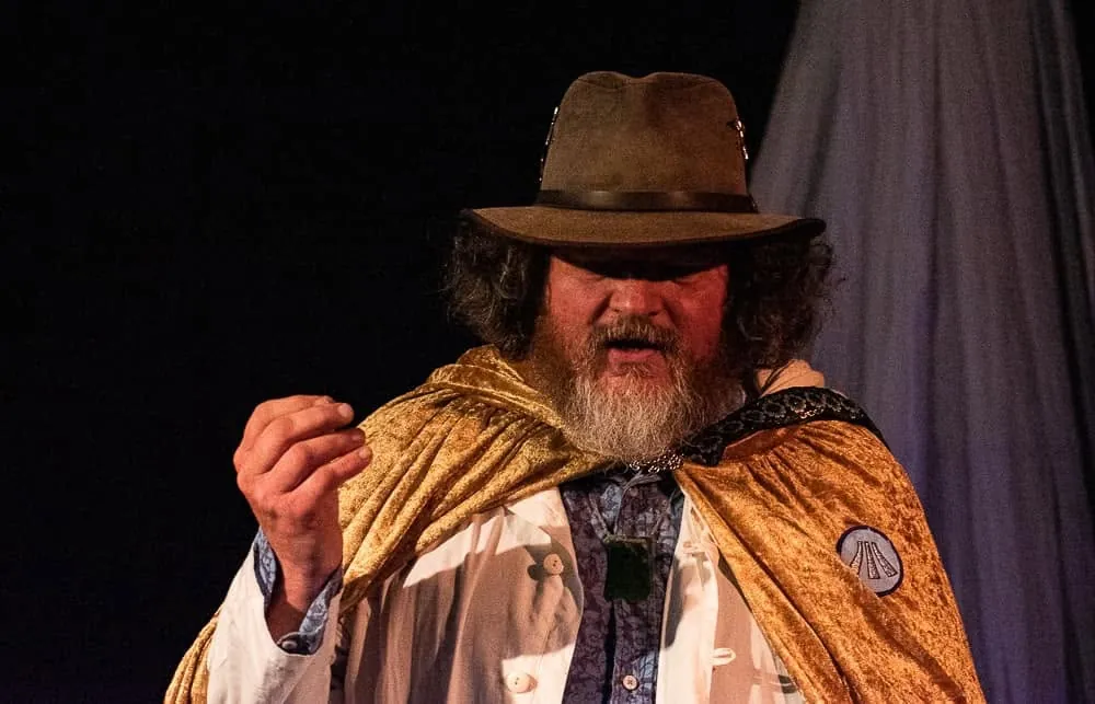 Tor Webster on stage mid-talk, in a hat and gold cloak